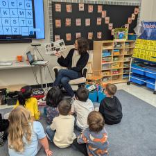 An Adult reads to a group of students sitting on the carpet in the classroom