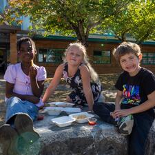 Three elementary students sitting on a rock, eating french fries.