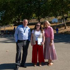 One male and two female staff stand near a basketball court and playground, posing for a photo.